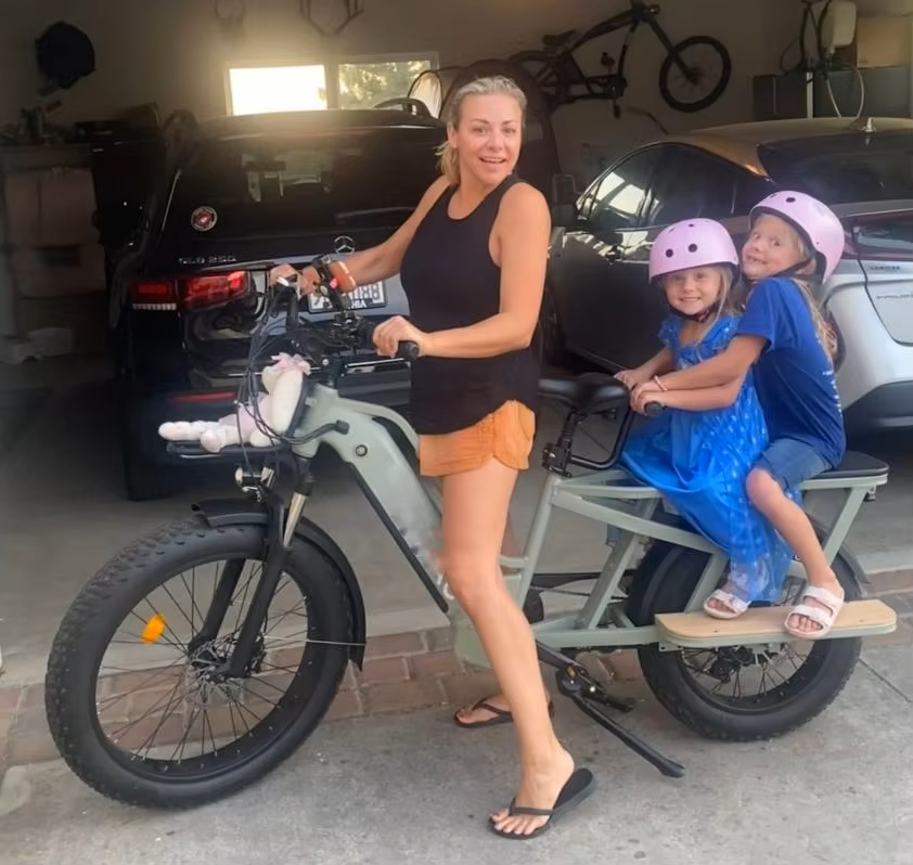Parent carrying two kids on eco-friendly electric cargo bike for school runs